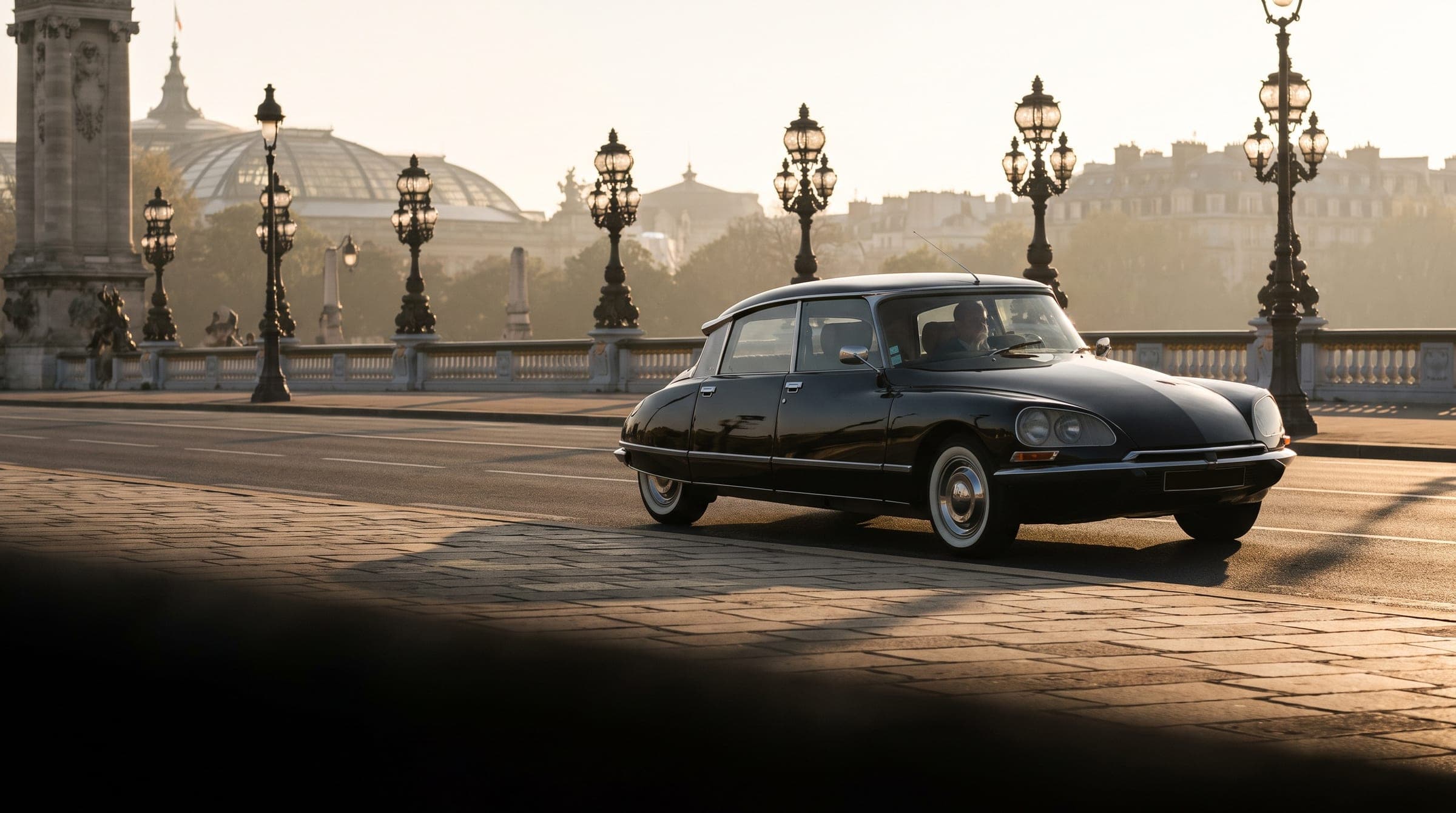 A black Citroën DS crossing a Paris bridge at sunrise
