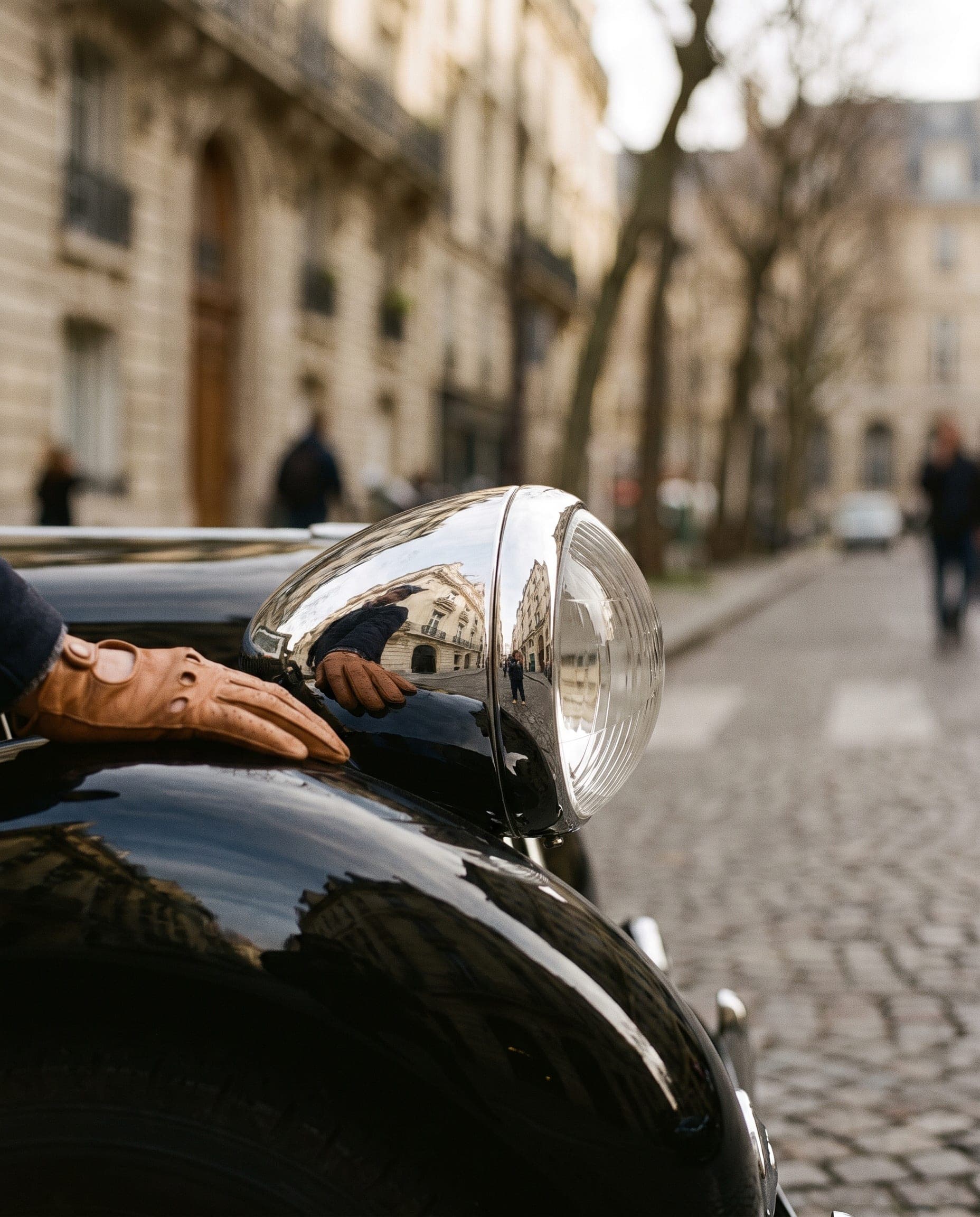 Eine behandschuhte Hand auf dem verchromten Scheinwerfer eines schwarzen Citroën Traction Avant